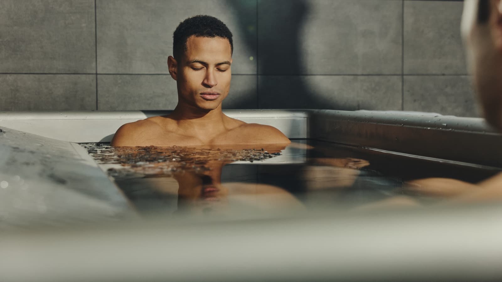 Gast mit Handtuch neben dem Cold Plunge, im Hintergrund zwei Gäste im Becken am Fenster