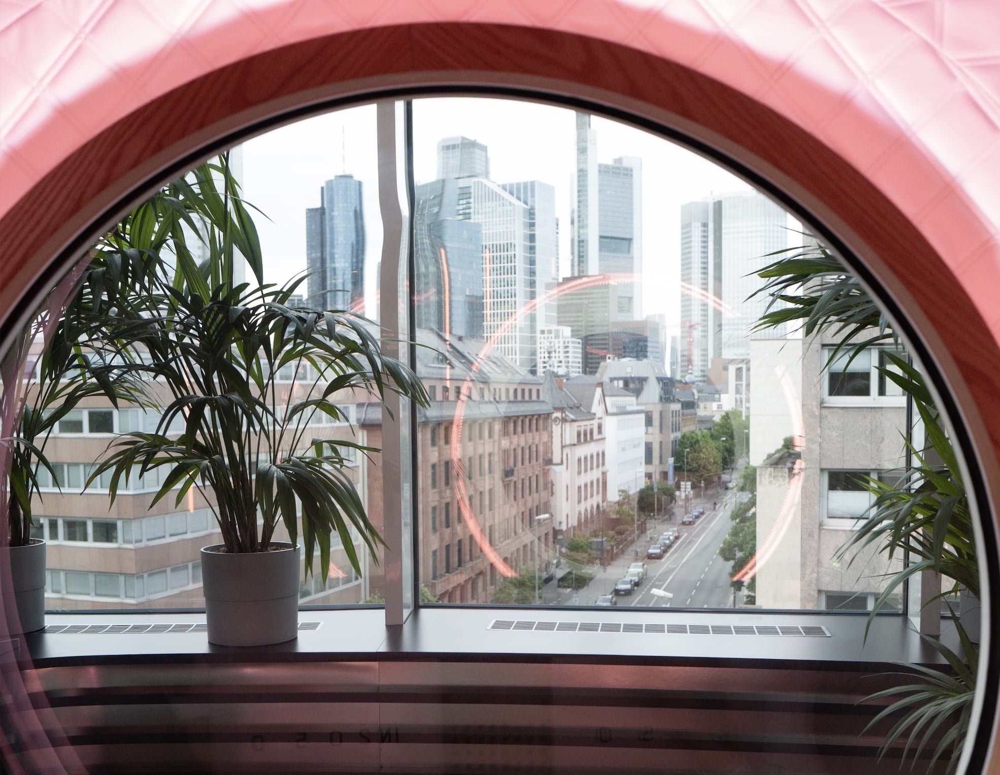 Rundes Fenster mit Pflanzen und Blick auf die Frankfurter Skyline, gerahmt vom Rot der Sauerstoffkammer